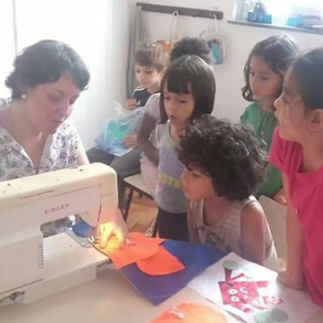 Ananda na máquina de costura com um grupo de crianças ao redor, acompanhando o trabalho