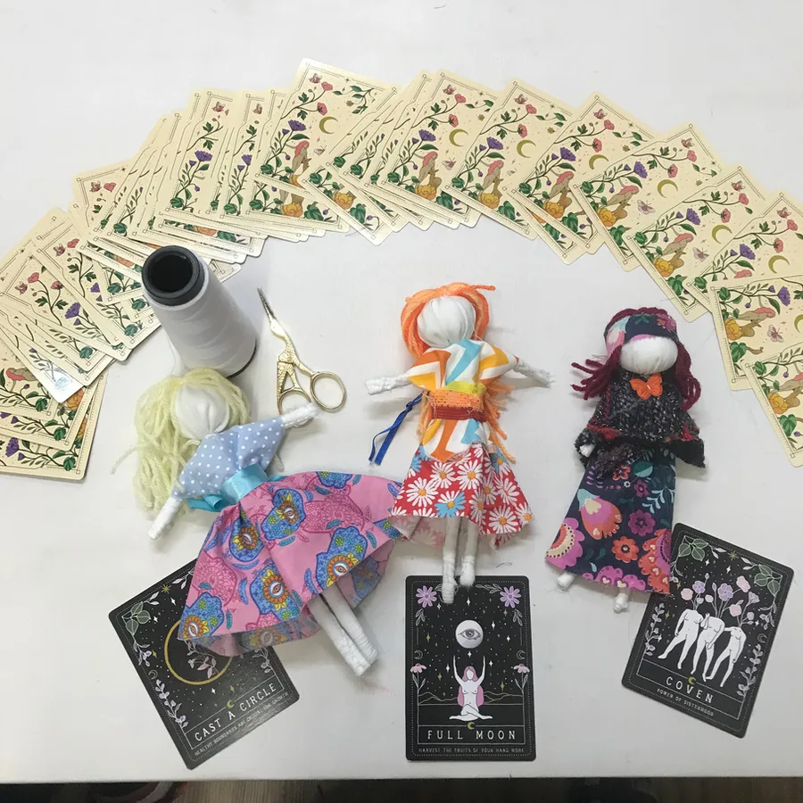 Bonecas de pano vestidas com tecidos estampados, dispostas sobre cartas e rendas