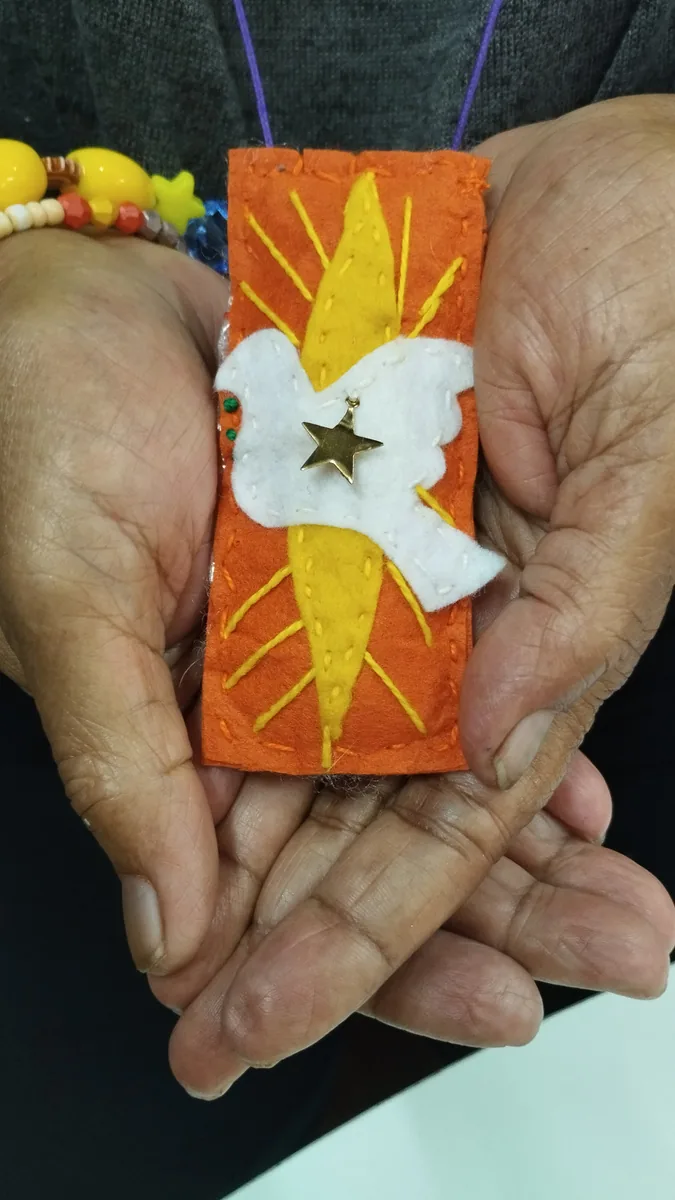 Mãos segurando um pequeno estandarte de feltro laranja bordado com uma estrela